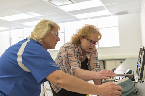Heather working with her instructor on an electrical training box.